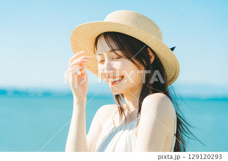 海と青空バックの麦わら帽子を被った女性 129120293