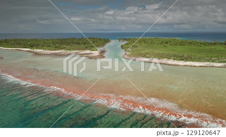 An aerial perspective reveals a stunning tropical setting with turquoise waters gently blending with orange hues, creating a picturesque shoreline bordered by lush greenery and white sand. 129120647