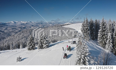 Aerial drone tourists riding snowmobiles and taking pictures in a snowy mountain forest, enjoying a breathtaking winter landscape on a sunny day. Bukovel ski resort. Winter travel background Aerial drone tourists riding snowmobiles and taking pictures in a snowy mountain forest, enjoying a breathtaking winter landscape on a sunny day. Bukovel ski resort. Winter travel background 129120720