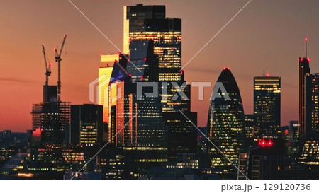 Warm sunset over London iconic skyline, featuring 30 St Mary Axe (The Gherkin), with construction cranes symbolizing growth in the bustling metropolis. Cityscape night background. Drone flight 129120736