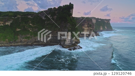 Aerial drone captures the breathtaking Uluwatu Temple perched atop a majestic cliff as waves crash against the rocks, creating a mesmerizing scene during a vibrant sunset Aerial drone captures the breathtaking Uluwatu Temple perched atop a majestic cliff as waves crash against the rocks, creating a mesmerizing scene during a vibrant sunset 129120746