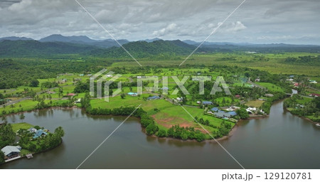 Drone capturing breathtaking scenery of Savusavu town featuring lush green landscape, meandering river, residential houses, and rolling hills in Fiji, showcasing tropical beauty and tranquility 129120781