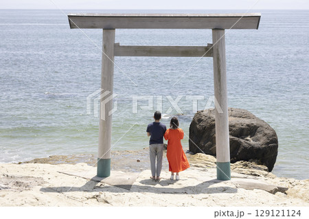 海岸沿いの鳥居の前に立つふたり 129121124