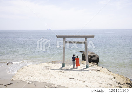 海岸沿いの鳥居の前に立つふたり 129121169