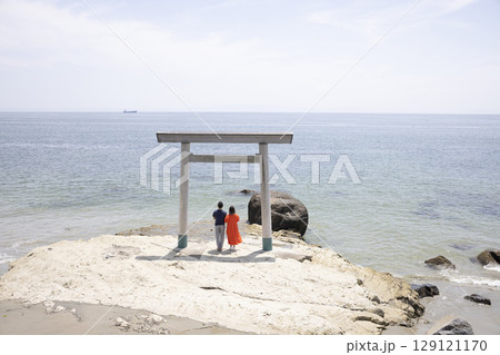 海岸沿いの鳥居の前に立つふたり 129121170