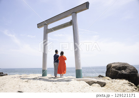 海岸沿いの鳥居の前に立つふたり 129121171