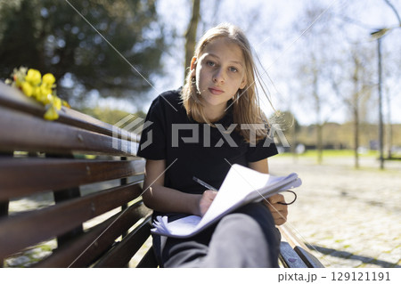 Young student studying outdoors on park bench taking notes Young student studying outdoors on park bench taking notes 129121191
