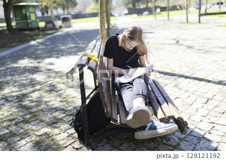 Young student girl doing homework sitting on bench in park 129121192