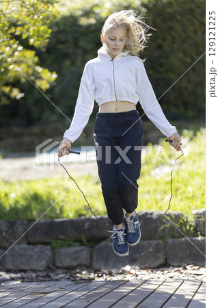 Young blonde girl jumping rope in a park wearing sporty outfit Young blonde girl jumping rope in a park wearing sporty outfit 129121225