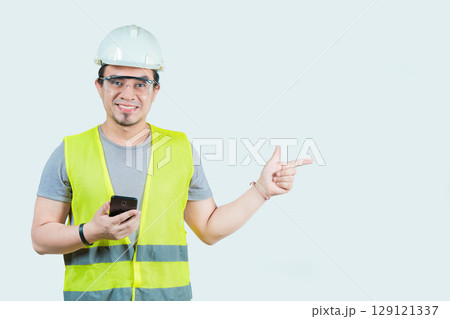 Handsome architect holding phone pointing at blank space isolated. Smiling young engineer holding smartphone and pointing at a blank space isolated 129121337