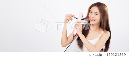 Hair styling with a hair straightener as an Asian woman smooths her long hair, showing beauty, confidence, and salon-like results in a home routine. isolated studio white background Hair styling with a hair straightener as an Asian woman smooths her long hair, showing beauty, confidence, and salon-like results in a home routine. isolated studio white background 129121889