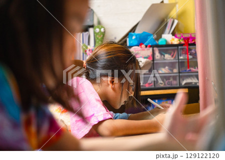 Two elementary school girls are studying at their desks at home. Two cute schoolgirls are diligently doing their homework. Two elementary school girls are studying at their desks at home. Two cute schoolgirls are diligently doing their homework. 129122120