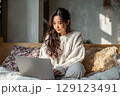 ベッドの上でリラックスしながらノートパソコンでリモートワークをしている若い女性 129123491