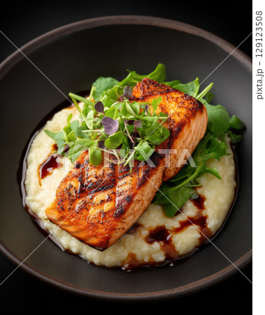 Grilled salmon on creamy risotto with fresh greens and balsamic glaze in dark bowl Grilled salmon on creamy risotto with fresh greens and balsamic glaze in dark bowl 129123508