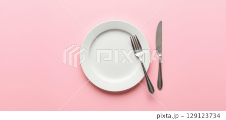 Empty white plate with fork and knife on pink background. Minimalist table setting, dining, restaurant, food preparation, and meal concept 129123734