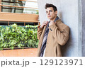 Stylish young man in coat and scarf outdoors 129123971