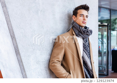 Stylish young man in coat and scarf outdoors 129123974