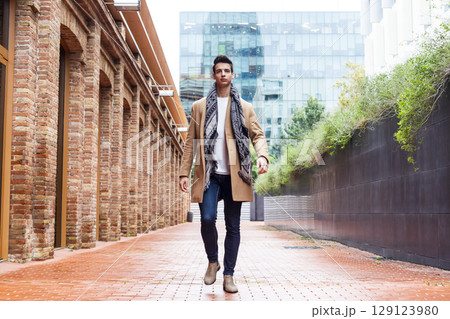 Confident man walking between brick and glass buildings 129123980