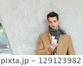 Stylish man texting on smartphone against concrete wall 129123982