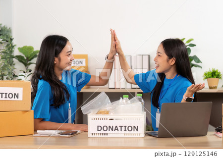 Volunteer teamwork. Two women collaborating on donation project with enthusiasm. Volunteer teamwork. Two women collaborating on donation project with enthusiasm. 129125146