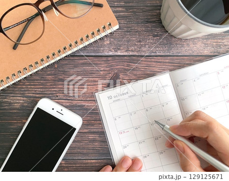 10月のスケジュール帳に記入する女性の手と机上のスマホ 129125671
