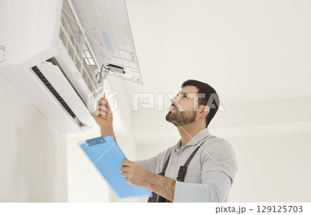 Technician with screwdriver checking air conditioner system and providing maintenance at client home Technician with screwdriver checking air conditioner system and providing maintenance at client home 129125703