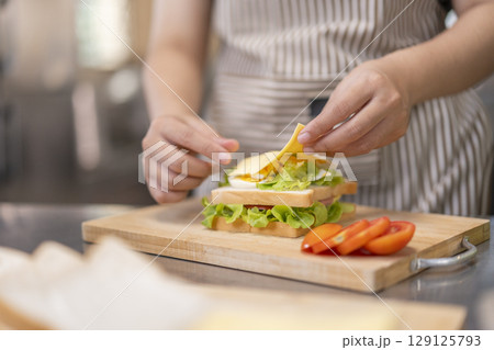 Hand placing slice of cheese on homemade sandwich. 129125793