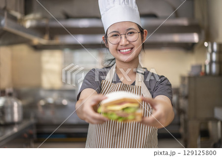 Smiling Asian Female Chef Holding Sandwich in Kitchen 129125800