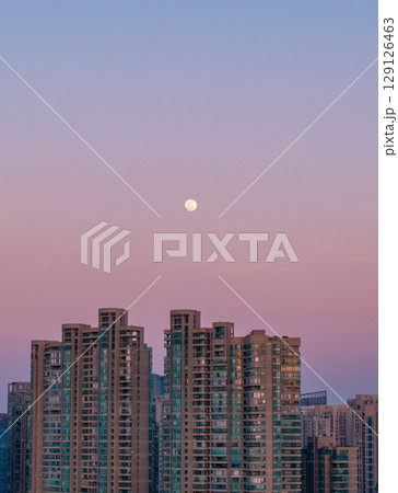 Evening skyline view of city with rising moon illuminating high-rise buildings at dusk Evening skyline view of city with rising moon illuminating high-rise buildings at dusk 129126463