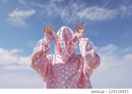A person wearing a pink hoodie with polka dots is standing in front of a blue sk 129126855