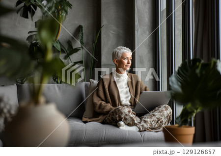 A woman is sitting on a couch with a laptop in front of her 129126857