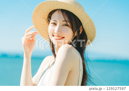 海と青空バックの麦わら帽子を被った女性 129127597
