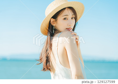 海と青空バックの麦わら帽子を被った女性 129127599