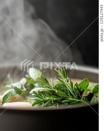 Close-up of fresh herbs steaming in a hot soup pot on dark background 129127945