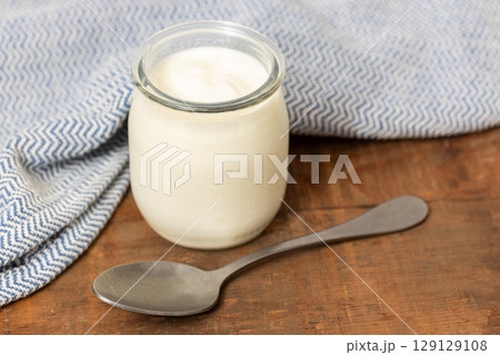 yogurt Glass jar on wooden table with spoon and blue cloth still life 129129108