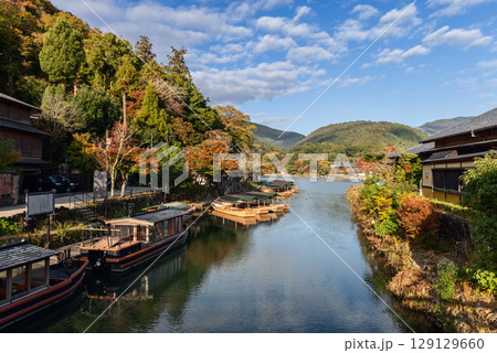 Wooden boats line the calm river in Arashiyama, Kyoto, Japan, with autumn trees on both banks Wooden boats line the calm river in Arashiyama, Kyoto, Japan, with autumn trees on both banks 129129660