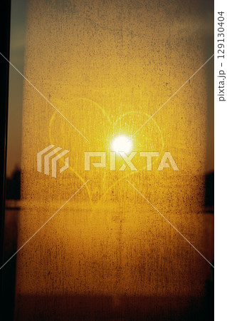 Heart shape drawn on foggy window at sunset with golden sun shining through glass Heart shape drawn on foggy window at sunset with golden sun shining through glass 129130404