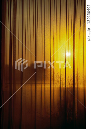 Golden sunset light shining through sheer curtains and foggy window indoors. 129130405