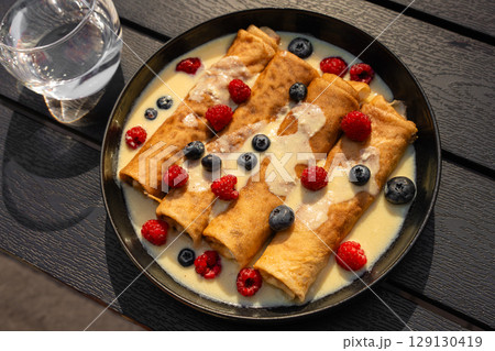 Delicious breakfast pancakes with vanilla sauce, raspberries and blueberries on black plate 129130419