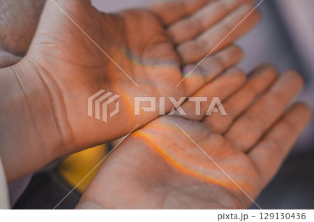 Close-up of childs open hands with soft rainbow light shining across the palms, a dreamy atmosphere. 129130436