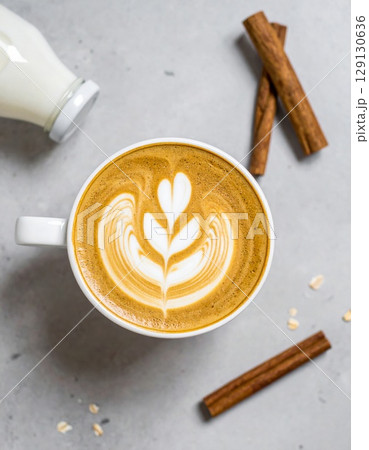 Overhead View of Latte Art in White Cup with Cinnamon Sticks and Bottle 129130636