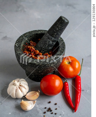 Granite Mortar with Pestle with Spicy Mixture and Raw Ingredients on Gray Surface 129130864