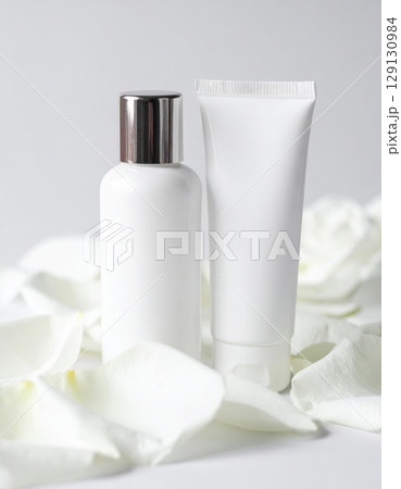 Two White Cosmetic Bottles Surrounded by White Rose Petals on Light Background 129130984