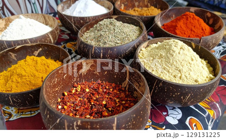 Assorted Colorful Spices and Herbs in Natural Coconut Shell Bowls on Patterned Tablecloth 129131225