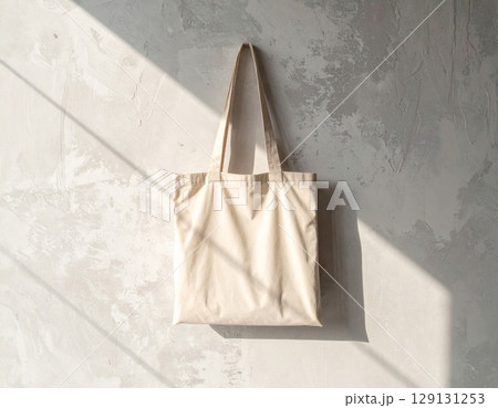 Beige Canvas Tote Bag Hanging on Concrete Wall with Sunlight and Shadows 129131253