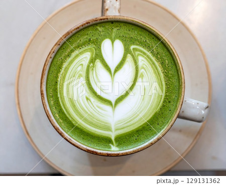 Overhead Shot of Green Matcha Latte Art in White Ceramic Cup on White Plate 129131362