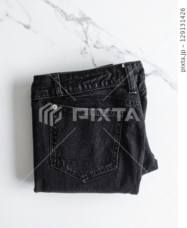 Folded Black Denim Jeans on White Marble Surface in Soft Lighting Folded Black Denim Jeans on White Marble Surface in Soft Lighting 129131426