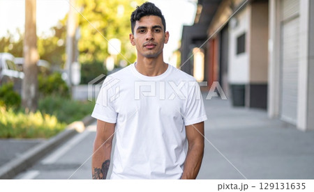 Portrait of a Young Man in White T-Shirt Walking on Sidewalk with Urban Background 129131635
