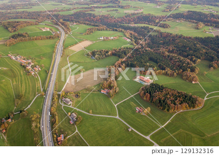 Aerial view of small scattered farm houses with red tiled roofs among green farming fields and distant forest in summer. 129132316
