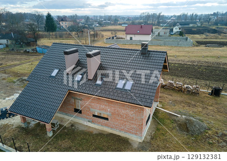 Aerial view of house roof top covered with ceramic shingles. Tiled covering of building under construction 129132381
